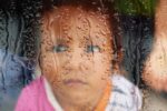 Trauriges Kind hinter verregneter Fensterscheibe