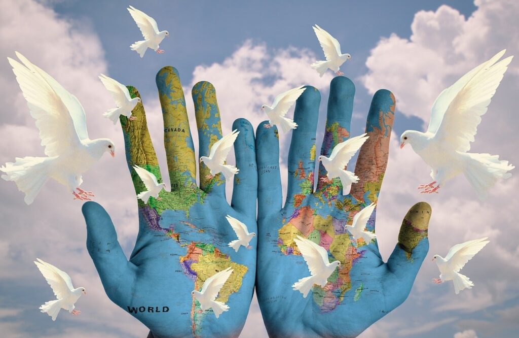 Weltfrieden (zahlreiche weiße Tauben vor dem Hintergrund aus zwei mit den Umrissen der Kontinente bemalten Händen und Wolken)