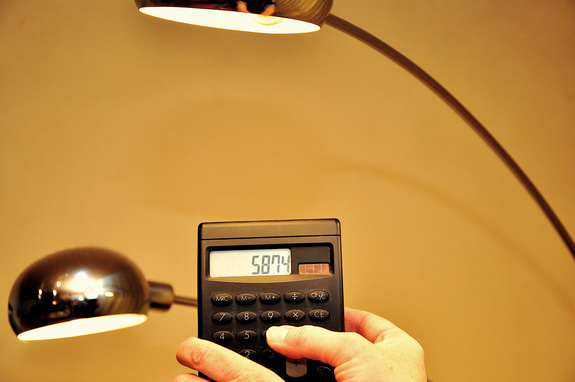 Symbolbild Energiesparen: Zwei von rechts nach links geneigte Schreibtischlampen leuchten. In der Mitte wird auf einem Taschenrechner die Zahl 5874 angezeigt.