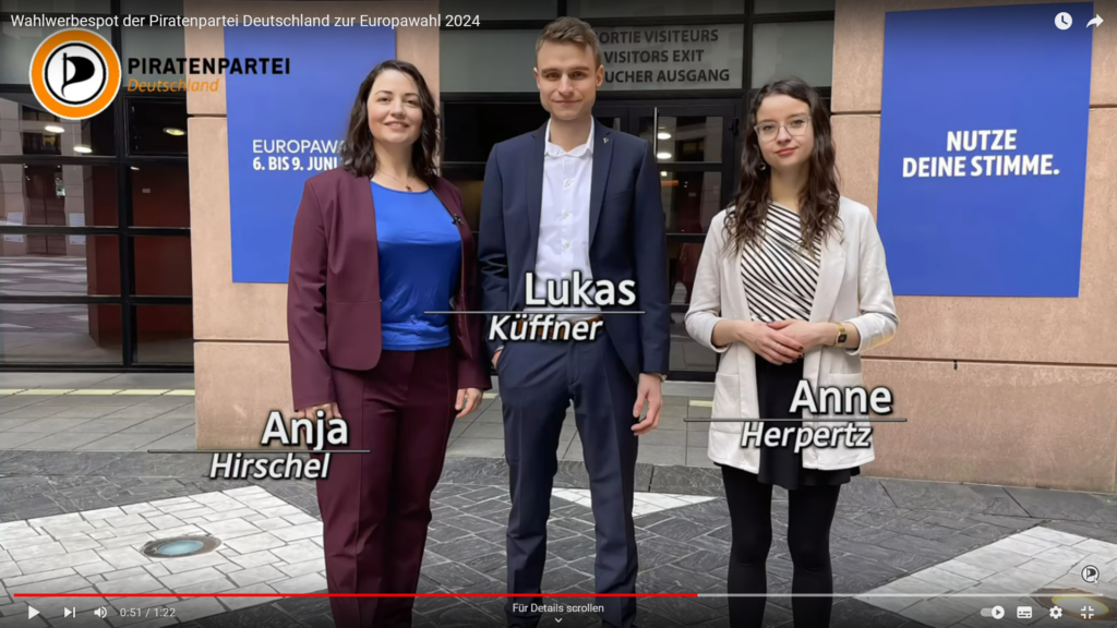 Screenshot aus dem Wahlwerbespot der Piratenpartei Deutschland zur Europawahl 2024. Im Bild sind die 3 Spitzenkandidaten zu sehen: Anja Hirschel (links), Anne Herperts (rechts), Lukas Küffner (Mitte). An den Kandidat:innen stehen ihre Namen, der Vorname fett und unterstrichen, darunter der Nachname. Im Hintergrund ist der Eingang zum Europäischen Parlament zu sehen. An der Wand sind links und rechtes zwei Plakate angebracht. Links steht "Europawahl 6.-9. Juni 2024", rechts steht "Nutze Deine Stimme.". Oben links ist das Logo der Piratenpartei Deutschland eingeblendet.